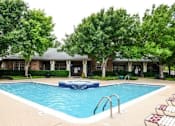 Thumbnail 4 of 31 - A swimming pool surrounded by trees and a building in the background.