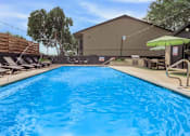 Thumbnail 6 of 31 - A large blue swimming pool with a wooden deck and sun loungers.