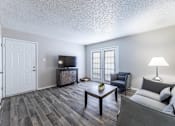 Thumbnail 6 of 10 - A living room with a grey couch, a wooden coffee table, and a television.