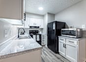 Thumbnail 1 of 10 - A kitchen with a black refrigerator and white cabinets.