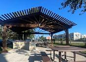 Thumbnail 3 of 14 - A wooden pergola with a table and chairs underneath it.