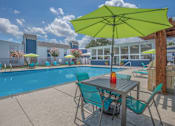 Thumbnail 5 of 14 - A table with a yellow umbrella is in the foreground of a pool area.