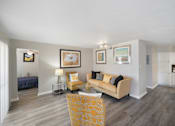 Thumbnail 9 of 15 - A living room with a yellow chair and a beige couch.