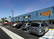 Thumbnail 8 of 77 - A silver car is parked in a parking lot in front of a blue building.