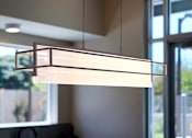 Thumbnail 46 of 77 - A modern light fixture hangs from the ceiling in a room with a view of the outdoors.