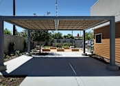 Thumbnail 19 of 77 - A patio with a white pergola and concrete floor.