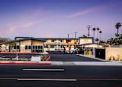 Thumbnail 13 of 21 - A building with a blue roof and white walls is surrounded by a fence and palm trees.