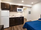Thumbnail 4 of 21 - A bedroom with a bed, sink, and refrigerator.