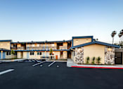 Thumbnail 12 of 21 - A parking lot in front of a building with a blue and beige exterior.