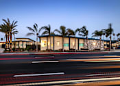 Thumbnail 4 of 37 - A building with palm trees in front of it at dusk.