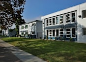 Thumbnail 1 of 2 - A white building with a blue trim is surrounded by a green lawn.