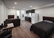 Thumbnail 88 of 116 - A modern bedroom with a large bed and a kitchen area in the background.
