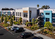 Thumbnail 60 of 116 - A parking lot with cars and a building with a blue and white facade.