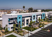 Thumbnail 55 of 116 - A modern building with a blue and white exterior is surrounded by a parking lot and other buildings.