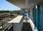 Thumbnail 45 of 116 - A long hallway with blue doors and a balcony overlooking a residential area.