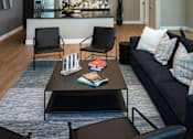 Thumbnail 32 of 116 - A modern living room with a black couch, a coffee table, and a kitchen area in the background.
