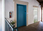 Thumbnail 29 of 36 - A blue door is in a white hallway.