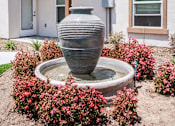 Thumbnail 14 of 36 - A grey vase is in the middle of a fountain surrounded by pink flowers.