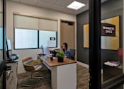 Thumbnail 84 of 114 - A woman is sitting at a desk in an office with a sign that says "Manager's Office" on the wall behind her.