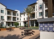 Thumbnail 61 of 114 - A courtyard with a palm tree and benches in front of a white building.