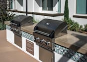Thumbnail 64 of 114 - Two black grills on a tan and white outdoor kitchen.