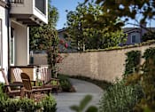 Thumbnail 46 of 114 - A concrete walkway leads to a house with a patio and chairs.