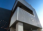 Thumbnail 26 of 103 - A modern building with a unique design featuring a series of white columns and a dark facade.