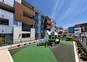 Thumbnail 8 of 103 - A playground area with a slide and green grass in front of apartment buildings.