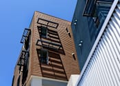 Thumbnail 6 of 103 - A building with a brown wooden facade and a white building with a corrugated metal facade.