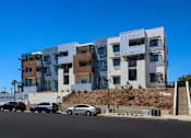 Thumbnail 78 of 103 - A modern multi-story building with a parking lot in front.