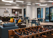 Thumbnail 31 of 103 - A foosball table is in the foreground of a room with a bar and seating area.