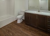Thumbnail 21 of 103 - A white toilet sits in a bathroom with wood floors and brown cabinets.