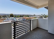 Thumbnail 82 of 103 - A balcony with a black railing overlooks a parking lot and buildings.