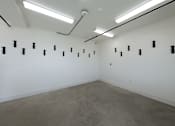 Thumbnail 96 of 103 - A room with a white wall and a grey floor with black objects on it.