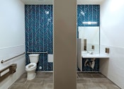 Thumbnail 77 of 103 - A bathroom with a toilet, sink, and a blue patterned wallpaper.