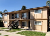 Thumbnail 9 of 9 - A beige two-story apartment building with a black metal staircase.