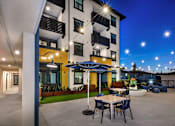 Thumbnail 80 of 94 - A patio area with tables and chairs is illuminated by lights at night.