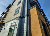 Thumbnail 89 of 94 - A tall building with a grey and yellow facade stands under a blue sky.