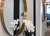 Thumbnail 70 of 94 - A round mirror with a gold frame is on a wooden table with a vase of white flowers.