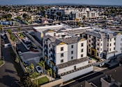 Thumbnail 11 of 94 - A large white building with a yellow section in the middle is surrounded by a parking lot.