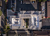 Thumbnail 12 of 94 - An aerial view of a building with a white facade and a red car parked in front.