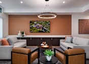 Thumbnail 80 of 90 - A modern living room with a grey sofa, a brown leather armchair, a coffee table with a plant and a painting on the wall.