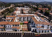 Thumbnail 62 of 90 - A large white building with a red roof is surrounded by parking lots.