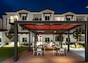 Thumbnail 69 of 90 - A patio with a table and chairs is illuminated by lights under a canopy.