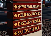 Thumbnail 31 of 90 - A signpost with multiple directional arrows pointing to various destinations such as Public Works, SMWD Water Plant, Police Services, Descanso Park, and Salida Del Sol.