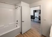 Thumbnail 18 of 90 - A white bathroom with a tub and a door leading to a living room.