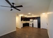 Thumbnail 9 of 25 - A room with a ceiling fan and a kitchen area in the background.