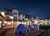 Thumbnail 35 of 61 - A playground area with a slide and a ball pit in front of apartment buildings at dusk.