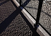 Thumbnail 1 of 61 - A black and white patterned fence casts a shadow on the ground.