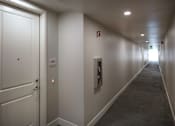 Thumbnail 58 of 61 - A long hallway with a door on the left and a fire extinguisher on the wall on the right.